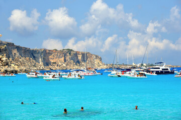Fototapeta na wymiar paradise clear torquoise blue water with boats and cloudy blue sky in background in Favignana island, Cala Rossa Beach, Sicily South Italy.