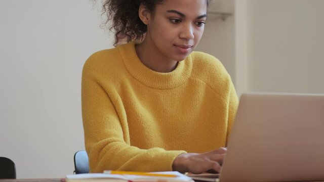 Concentrated african attractive woman using laptop computer while sitting by the table indoors