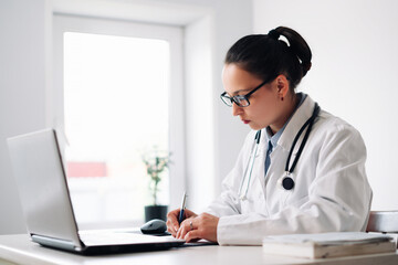 female doctor at her workplace with laptop and clipboard