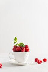 Fresh ripe raspberries in a white cup on white background. Side view, copy space. Natural cosmetics. Summer background, greeting card, poster, menu, cookbook