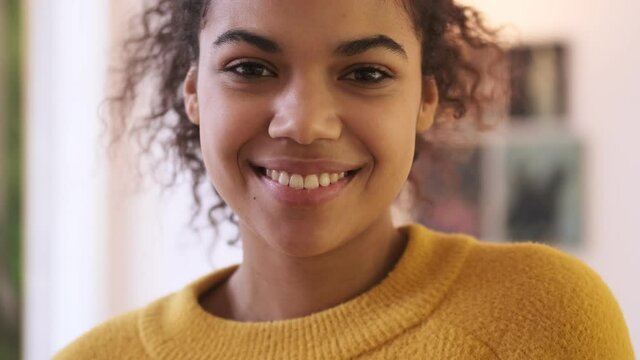 Close up view of Happy playful african attractive woman in yellow sweater opening her eyes and looking at the camera in living room