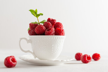 Fresh sweet raspberries in a white cup on white background. Side view, close up. Natural cosmetics, food background. Summer snack. Poster, greeting card
