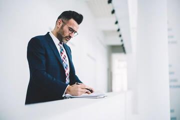 Pensive mature entrepreneur dressed in formal wear checking financial documents working in office interior.Confident proud ceo middle aged reading information and signing accounting reports