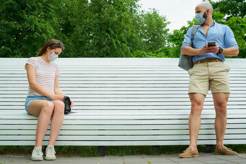 A man waiting near a bench keeping a social distance from a woman who sitting on a bench to avoid...