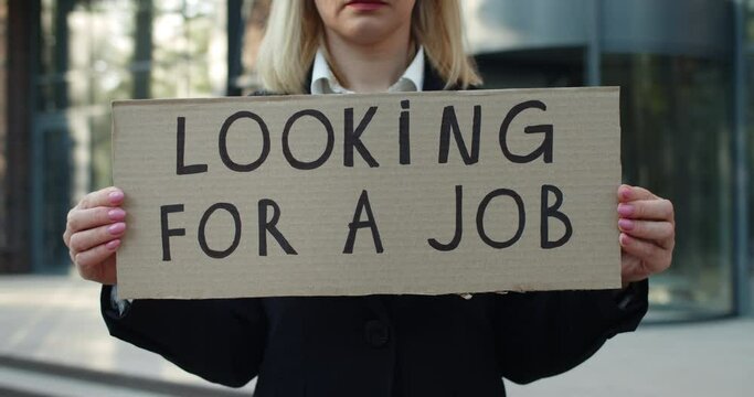 Crop view of workless female employee after pandemic lockdown. Woman in 30s showing carton with with looking for job writing while standing at street and looking to camera