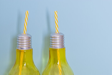festive glass drink on a blue background. glass in shape of a lightbulb with yellow striped straw. happy background with copy space.