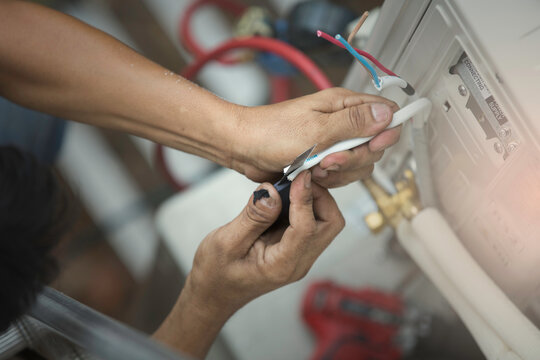 a professional electrician man is fixingand wiring a heavy duty unit of central air conditioning system by his tools.