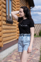 attractive young brunette woman in black t-shirt and denim shorts next to a wooden modern house. High quality photo
