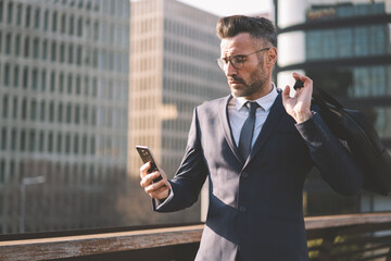 Concentrated matured businessman dressed in formal elegant suit checking email box texting feedback...
