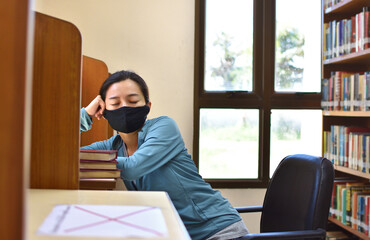 Female student wearing face mask sleeping in a university library