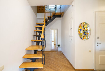 Modern interior of entrance hall in luxury apartment. Wooden stairs to the second floor. Mirror on...