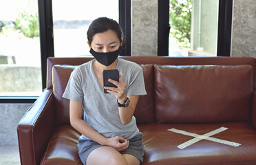 Young woman with mask using phone and sitting with distance for one seat from other people at the cafe