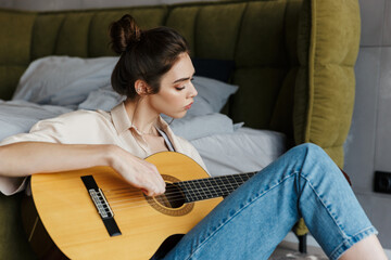 Image of young caucasian brunette woman playing acoustic guitar at home