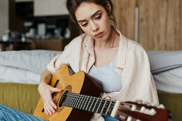 Image of young caucasian brunette woman playing acoustic guitar at home