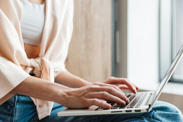 Naklejka premium Cropped image of woman working with laptop while sitting on floor