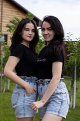 Obraz premium Two young brunette women in a black T-shirt and denim shorts hugging. Sisters, girlfriends. family and friendship concept. High quality photo