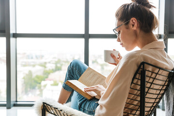 Image of thinking cute woman reading book and drinking coffee