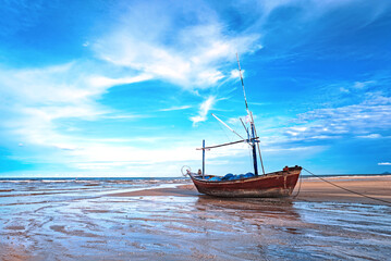 Old small fishing boat moor on the beach after low tide with beautiful blue sky background.