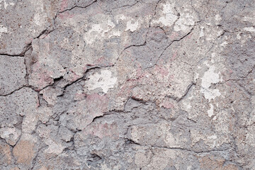 Fragment of an old weathered stone wall with cracks and chips. Partially chipped plaster