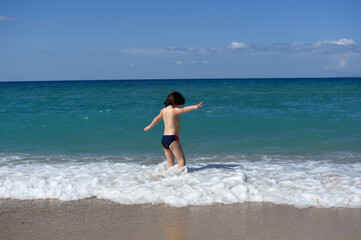 Fototapeta premium Little boy enjoying on beach. Child sit on beach and play in sea on summer vacation