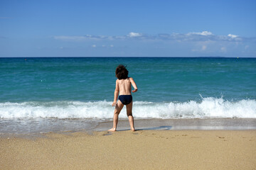 Little boy enjoying on beach. Child sit on beach and play in sea on summer vacation