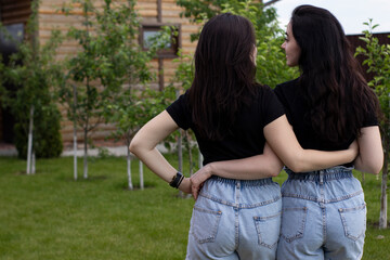 Fototapeta premium Two young brunette women in a black T-shirt and denim shorts hugging. Sisters, girlfriends. family and friendship concept. High quality photo