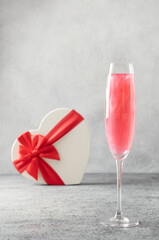 Shimmer edible glitter sparkling wine in two glasses with gift shaped of heart on grey. Close up.