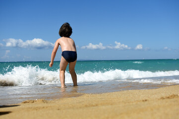 Fototapeta premium Little boy enjoying on beach. Child sit on beach and play in sea on summer vacation