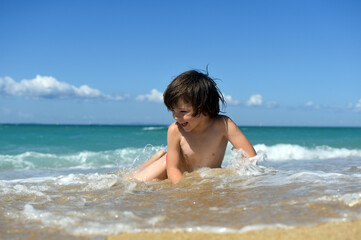 Little boy enjoying on beach. Child sit on beach and play in sea on summer vacation