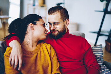 Fototapeta premium Positive young family marriage looking at each other with love spending free time together,romantic couple in love resting at cozy home interior , casually dressed hipster guy embrace his girlfriend.