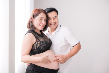 Fototapeta premium Asia young husband and young pregnant wife, standing and catch her belly