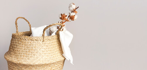 Straw wicker basket, natural cotton fabric, cotton flower branch on gray background. Bamboo basket...