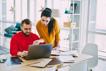 Male and female colleagues watching webinar together on laptop computer cooperating on project, coworkers searching information on website making online research consulting with each other in office.