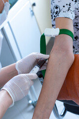 a nurse with a syringe takes venous blood for analysis , the patient's hand is compressed with a medical tourniquet,