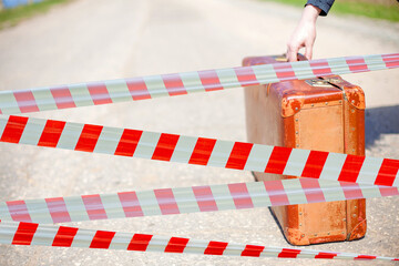 Fototapeta premium Restrictive tape. Traveler and brown suitcase on deserted road. Summer for travel. Time to rest.