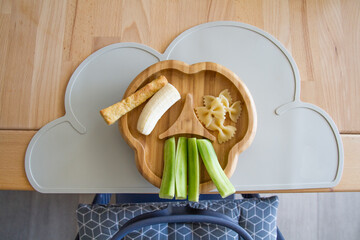 Plate (bamboo) with finger food (cucumber, pasta, banana) for babies in top view, showing the concept of baby-led weaning, nutrition without pureed food