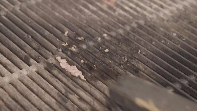 Close up of barbecue flames of the barbecue, and an iron brush cleaning the iron bars of the grill from the remains of an hamburger recently cooked. 
