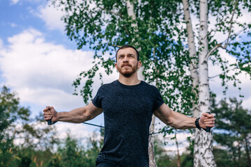Young handsome man exercising with rubber tape on nature on back
