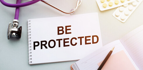 BE PROTECTED text written in a notebook on table with tablets and stethoscope, medical concept