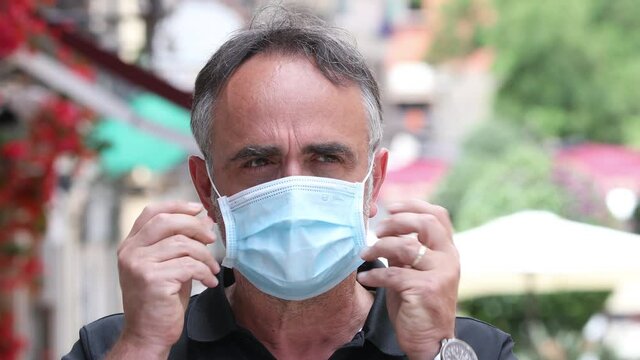 Ritratto di uomo bianco  che si mette una mascherina chirurgica in una strada del centro