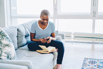 Young african american woman using mobile phone connected to wireless internet at home checking...