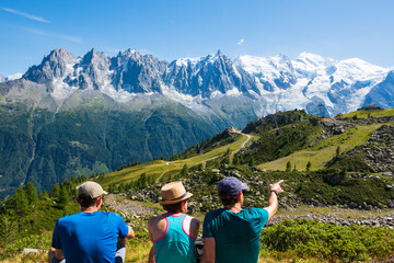 Fototapeta na wymiar French Alps summer travel. Three friends (unidentified people, back view) admiring beautiful snow covered Mont Blanc mountains range. France nature hiking tourism background. Active vacation concept