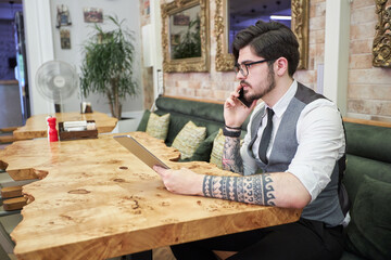Handsome elegant businessman sitting at reastaurant and reading on tablet.