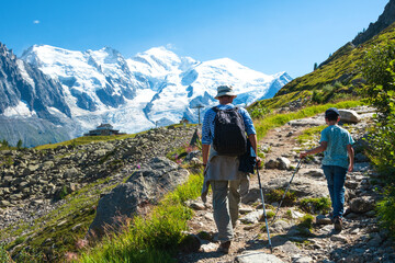 Father and son hiking in French Alps in summer. Back view. Snow covered Mont Blanc mountain and Plan Praz cable car station at background. Active holidays at nature concept.