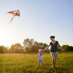Mom with her little son fly a kite in the meadow.