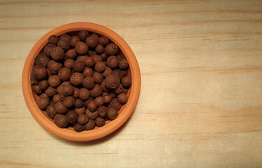 Allspice, pepper or pimento in clay bowl on wooden surface with copy space