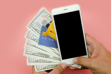 Close-up of woman hold money US dollars and using credit card and blank phone on pink background. - financial concept.