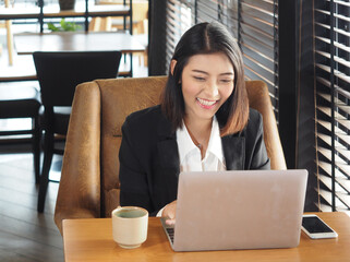 Asian business woman in suit is sittting with laptop computer and smile.
