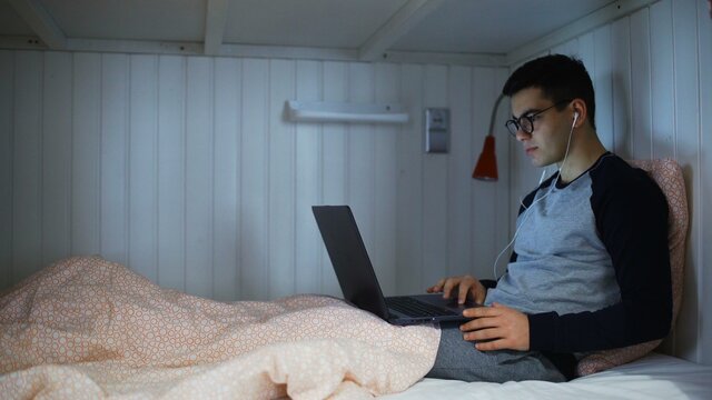 Young Man Working On Laptop At The Bed In Hostel Room