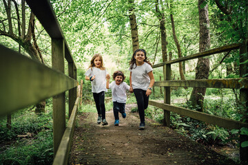 Three brothers running happily across a forest bridge